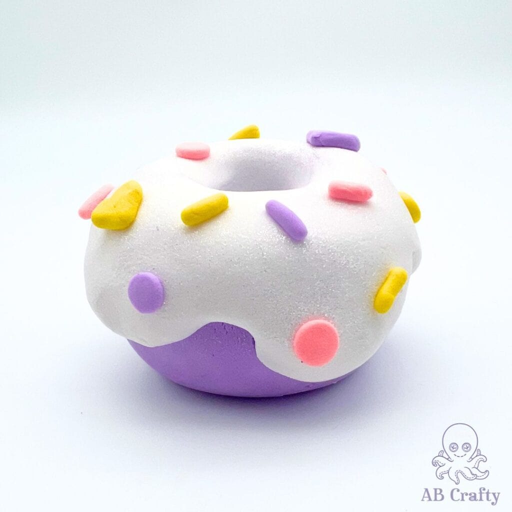 purple donut with white glitter frosting with yellow, pink, and purple sprinkles made from airdry clay from claymoo