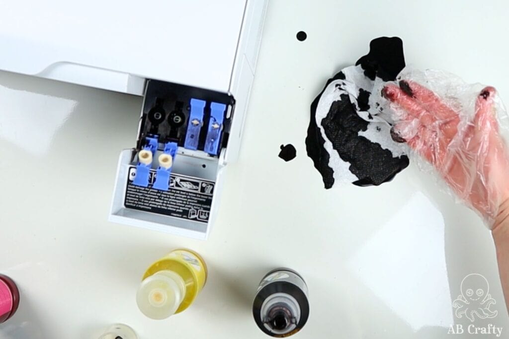 open tank of an epson ecotank printer with black sublimation ink all over it and the table