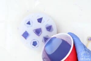 pouring purple epoxy resin into a lets resin dice mold from a solo cup