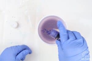 tapping let's resin purple mica powder into a cup with resin while wearing nitrile gloves