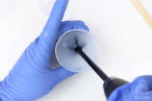 using an electric resin mixer to mix silicone in a small measuring cup while wearing nitrile gloves