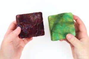 hands holding two felted soap bars - one is dark red with silk fibers and the other is various shades of green
